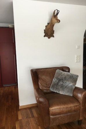 Un fauteuil en cuir marron avec un plaid en fourrure, une tête d’animal empaillée accrochée au mur et un plancher en bois.
