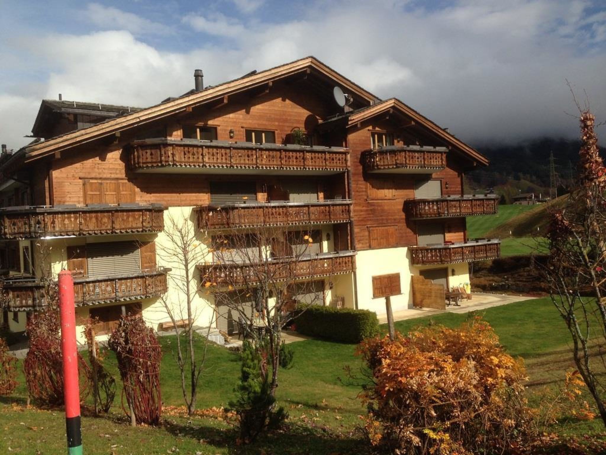 A multi-story wooden chalet with balconies, a satellite dish, and a well-maintained lawn.
