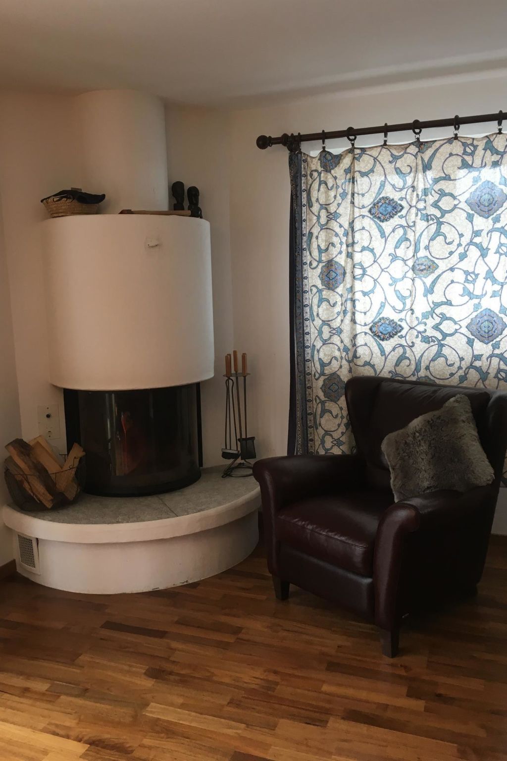 A living room with a fireplace, a leather armchair, and a patterned curtain.
