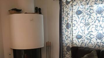 Un salon avec une cheminée, un fauteuil en cuir et un rideau à motifs.