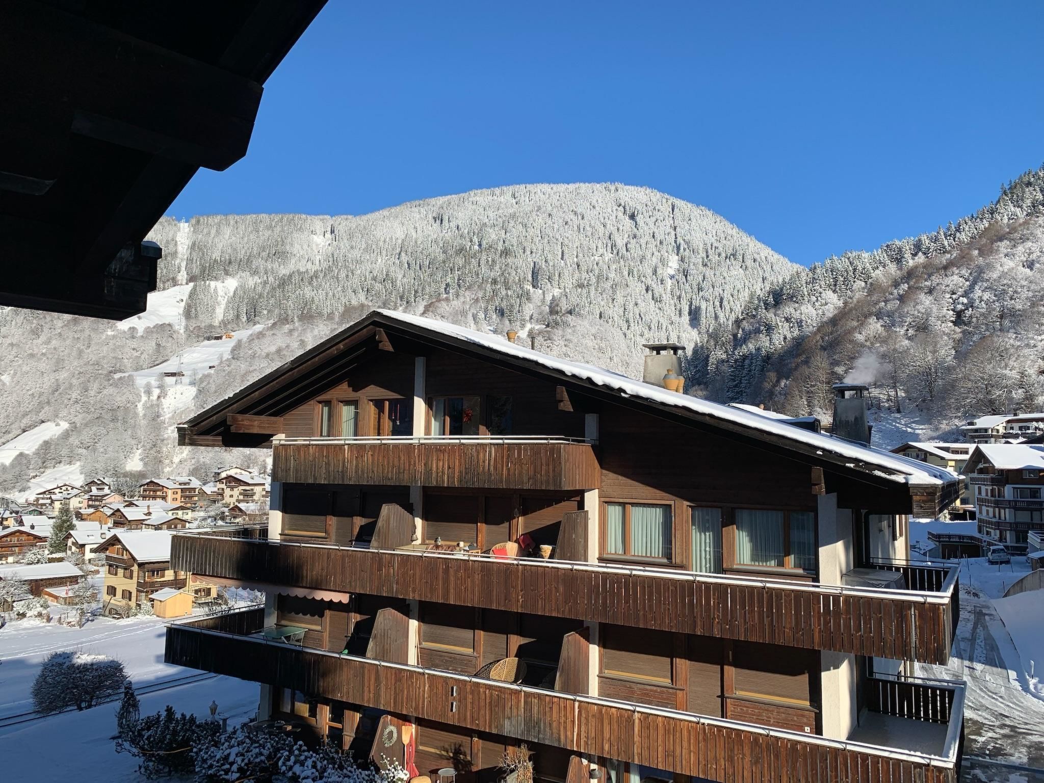 Eine Holzhütte mit mehreren Balkonen vor einer verschneiten Berglandschaft.