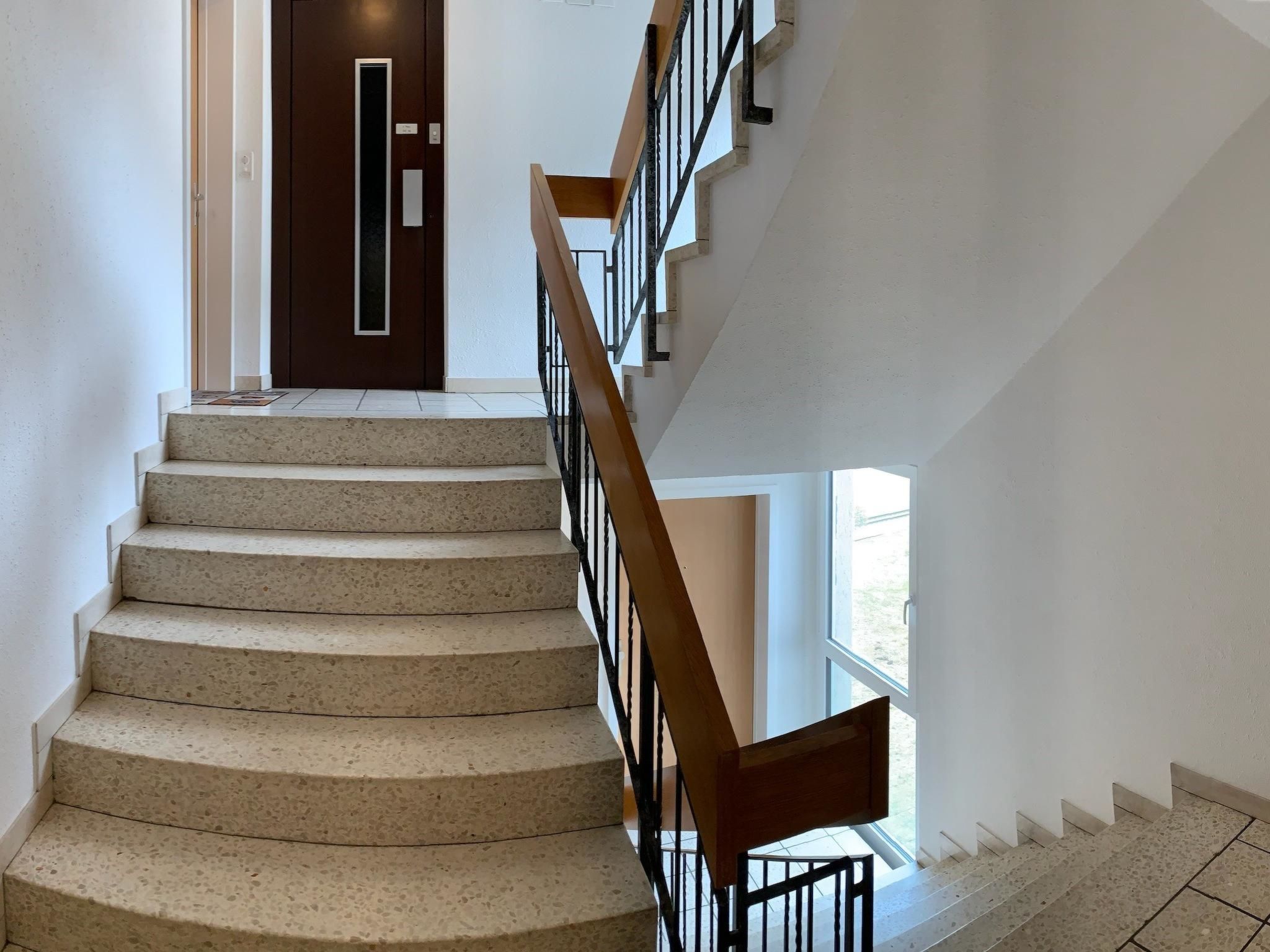Eine Treppe mit Handlauf, die zu einer Tür mit vertikalem Griff führt.