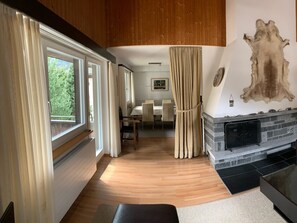 Ein modernes Interieur mit Kamin, Holzboden und einem Essbereich mit Blick auf die grüne Umgebung.