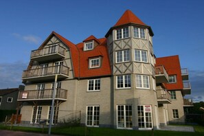 A multi-story building with a distinctive corner tower, balconies, and a red roof. - Holiday apartment with 1 bedroom (Cadzand)