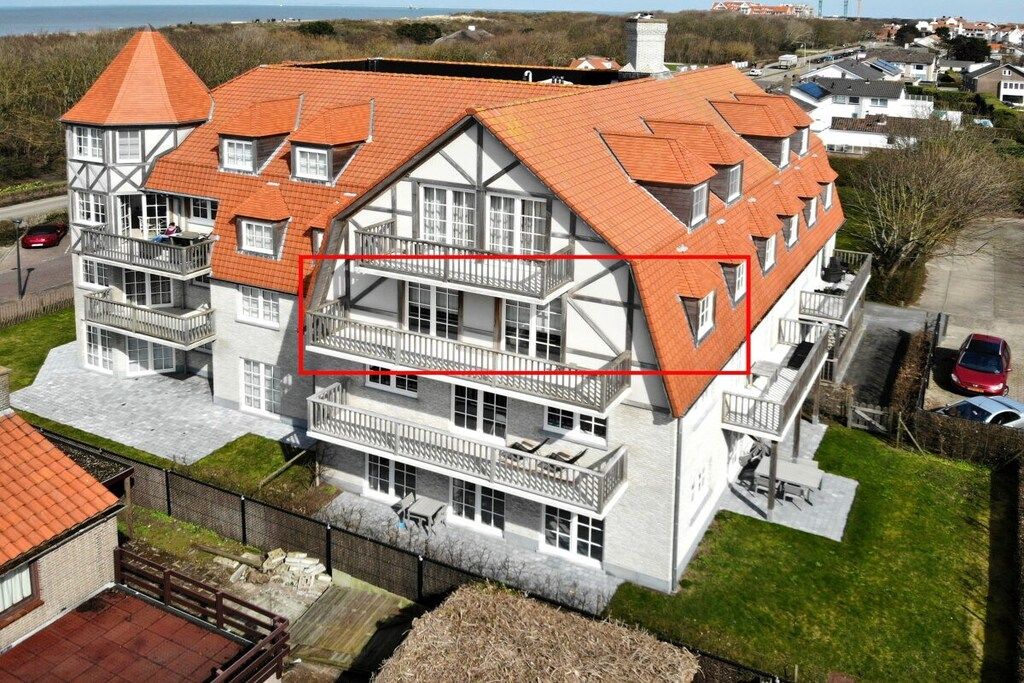 Een meerhoog gebouw met een opvallend balkon op de tweede verdieping, een rode pannendak en een uitzicht op de omgeving.