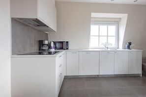A modern kitchen with white cabinetry, a built-in microwave, and a window providing natural light. - Holiday apartment with 1 bedroom (Cadzand)