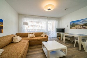 A living room with a sofa, coffee table, TV, and a dining area with chairs and a table. - Holiday apartment 27 Rogmans (Borkum)