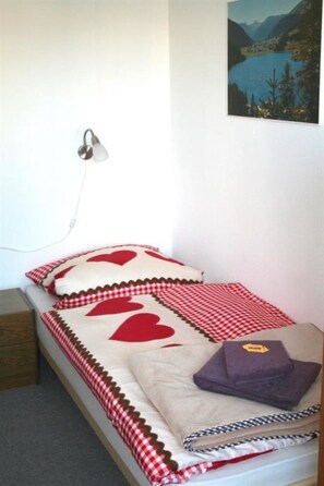 Una cama individual con colcha a cuadros rojos y blancos, un cojín con diseño de corazón y un cojín morado encima.