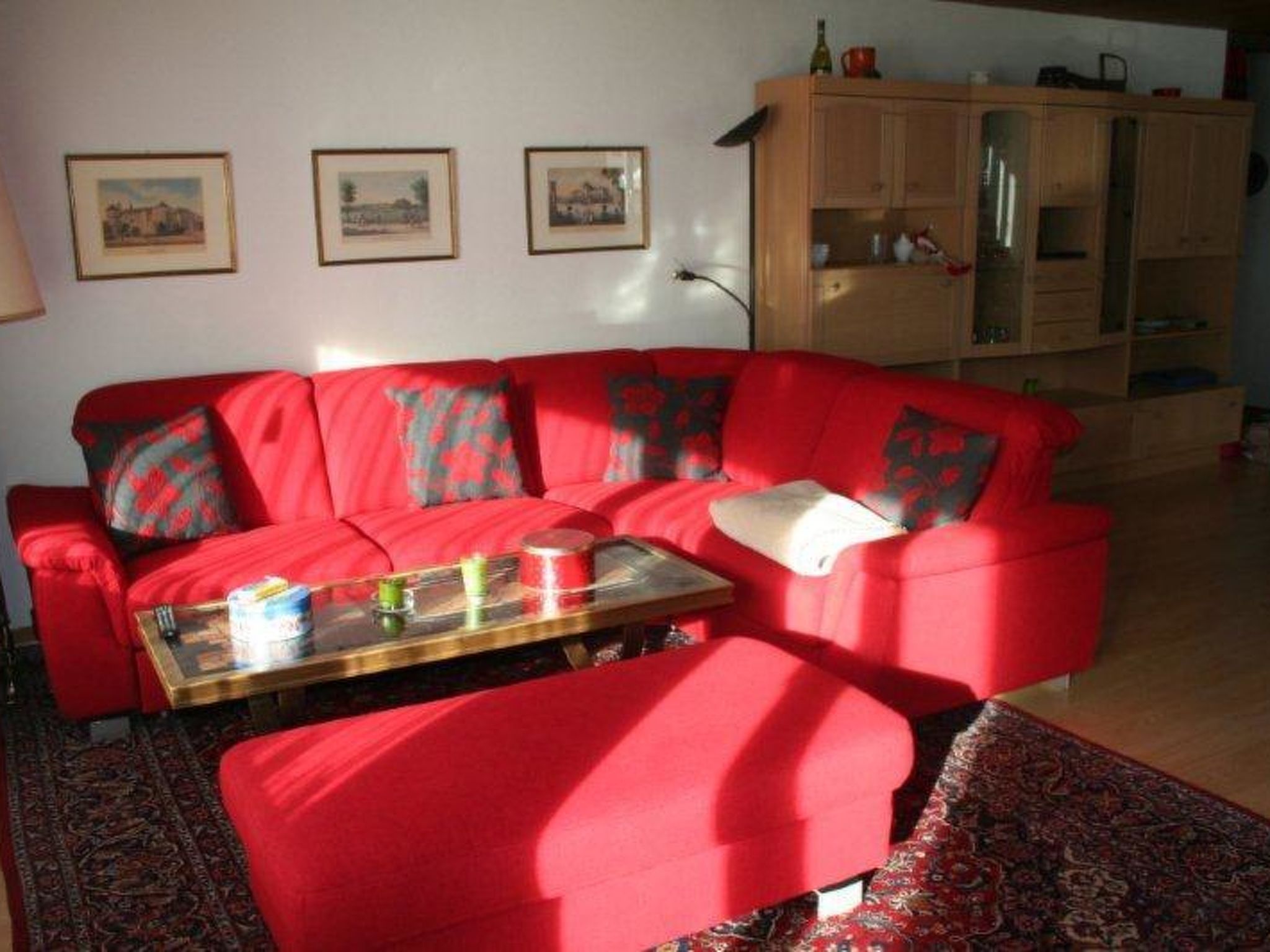 Un canapé rouge avec des coussins à motifs, une table basse en verre sur laquelle sont posés divers objets, et un tapis à motifs sur le sol.