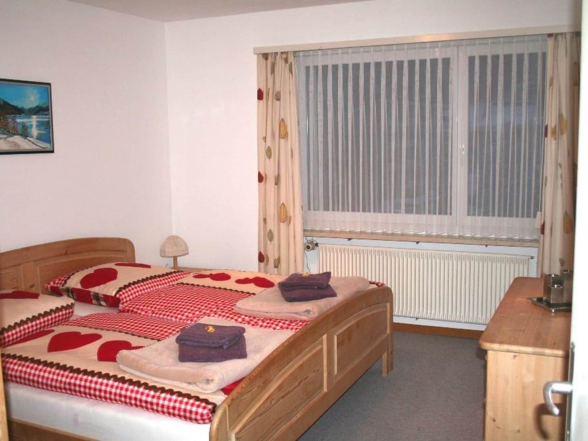 Un dormitorio con cama, mesita de noche, lámpara, ventana con cortinas y radiador.