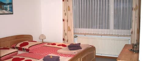 Un dormitorio con cama, mesita de noche, lámpara, ventana con cortinas y radiador.