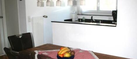 Un coin repas avec une table en bois, des chaises et un panier de fruits.
