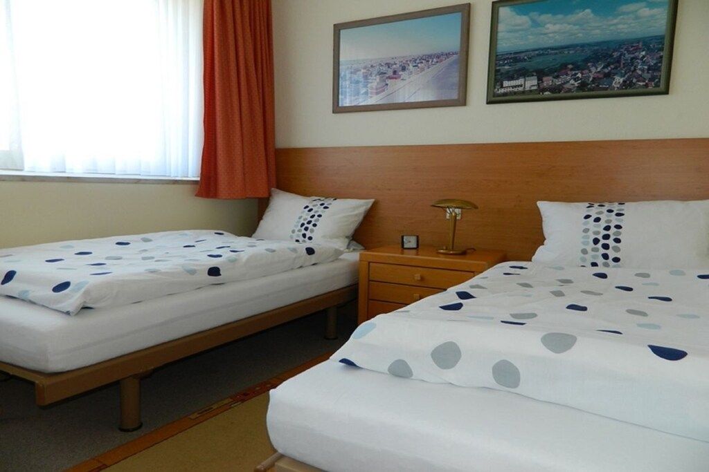 A hotel room with two single beds, a nightstand, a lamp, and two framed pictures on the wall.