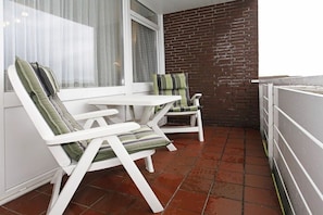 A small balcony with two white lounge chairs, one with a striped cushion and the other with a solid color cushion. - Holiday apartment with 1 bedroom (Borkum)
