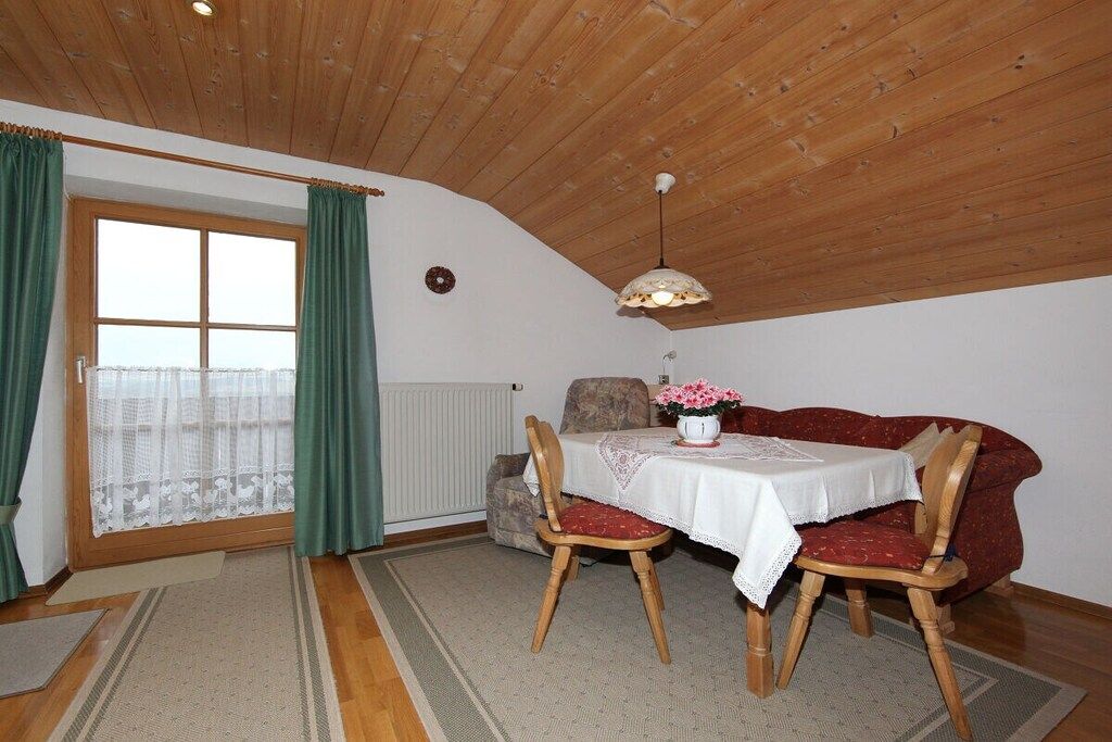 A cozy dining area with a table set for two, wooden chairs, a red sofa, and a window with curtains.