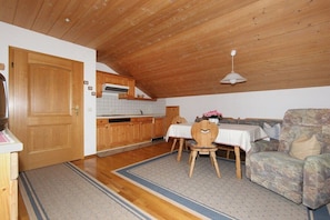 Ein gemütliches Zimmer mit Holzboden, einem Esstisch mit Stühlen, einer Couch und einer Küchenzeile mit Holzschränken und einer gefliesten Spritzschutzwand.