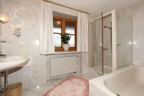 Ein Badezimmer mit einer Badewanne, einer Dusche, einem Waschbecken und einem Fenster mit Vorhängen.