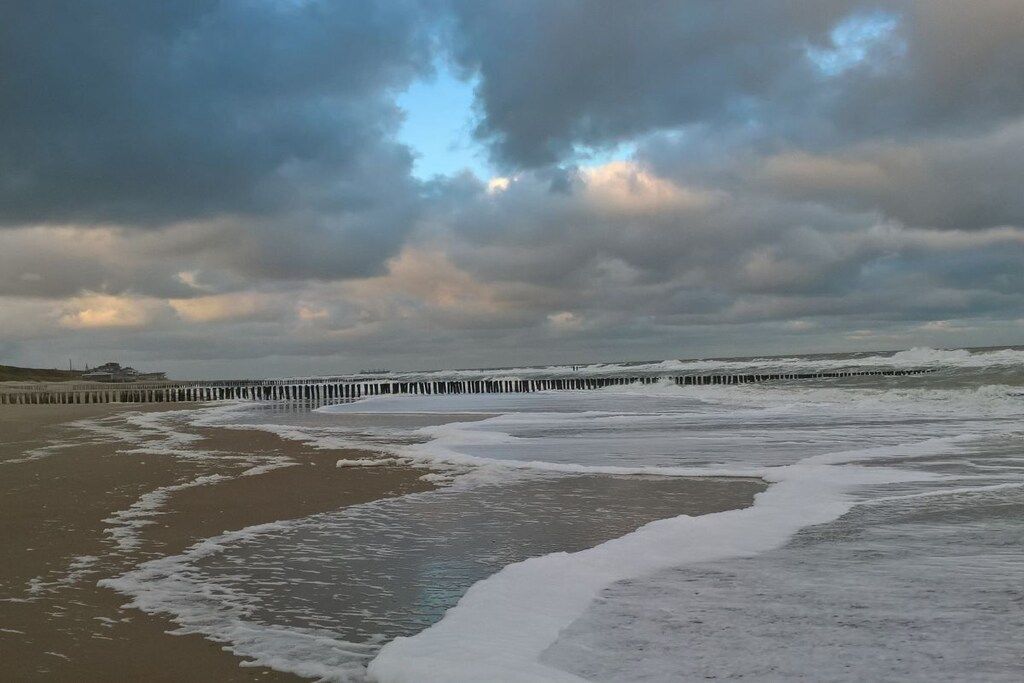 Ein Strand mit Wellen und einem Steg, der sich ins Wasser erstreckt.