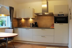 A modern kitchen with white cabinets, a stainless steel range hood, and built-in appliances. - Holiday apartment with 1 bedroom (Oostkapelle)