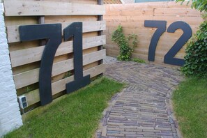A wooden fence with large numbers 71 and 72, a stone pathway, and a small grassy area. - Holiday apartment with 1 bedroom (Oostkapelle)
