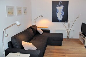 A modern living room with a sectional sofa, a flat-screen TV, and artwork on the walls. - Holiday apartment with 1 bedroom (Oostkapelle)