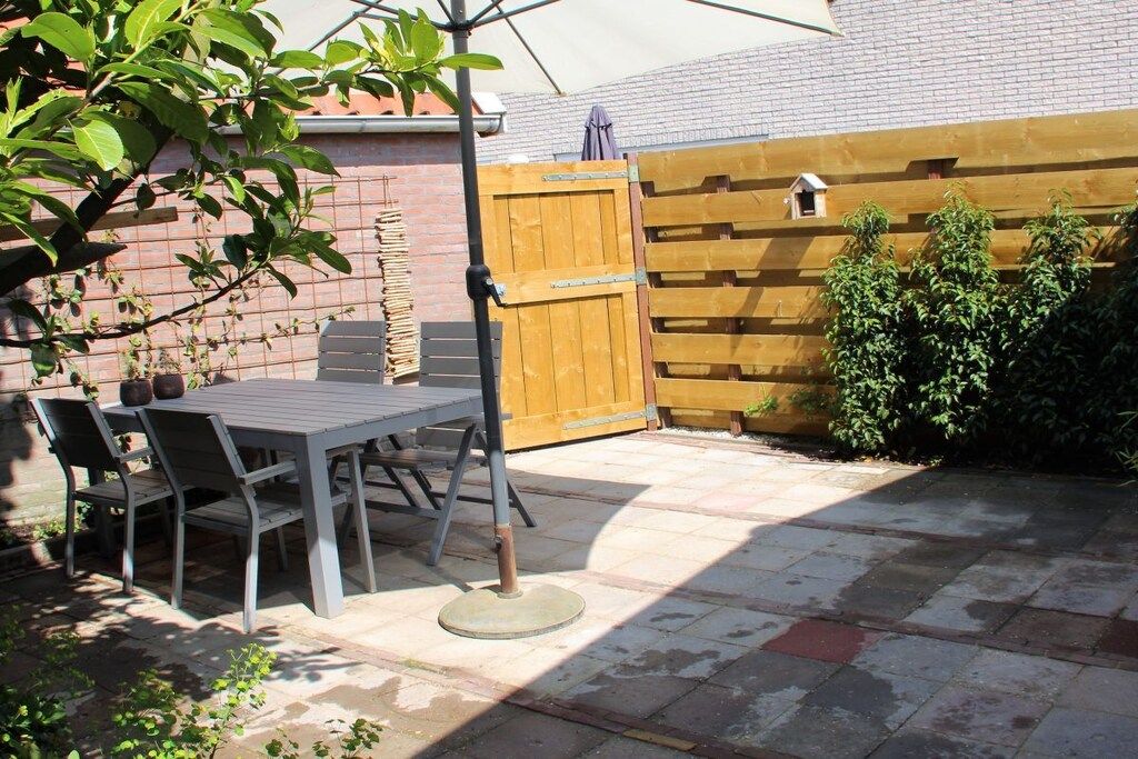 Eine Gartenlaube mit Tisch und Stühlen, einem Holzzaun und einem kleinen Vogelhäuschen.