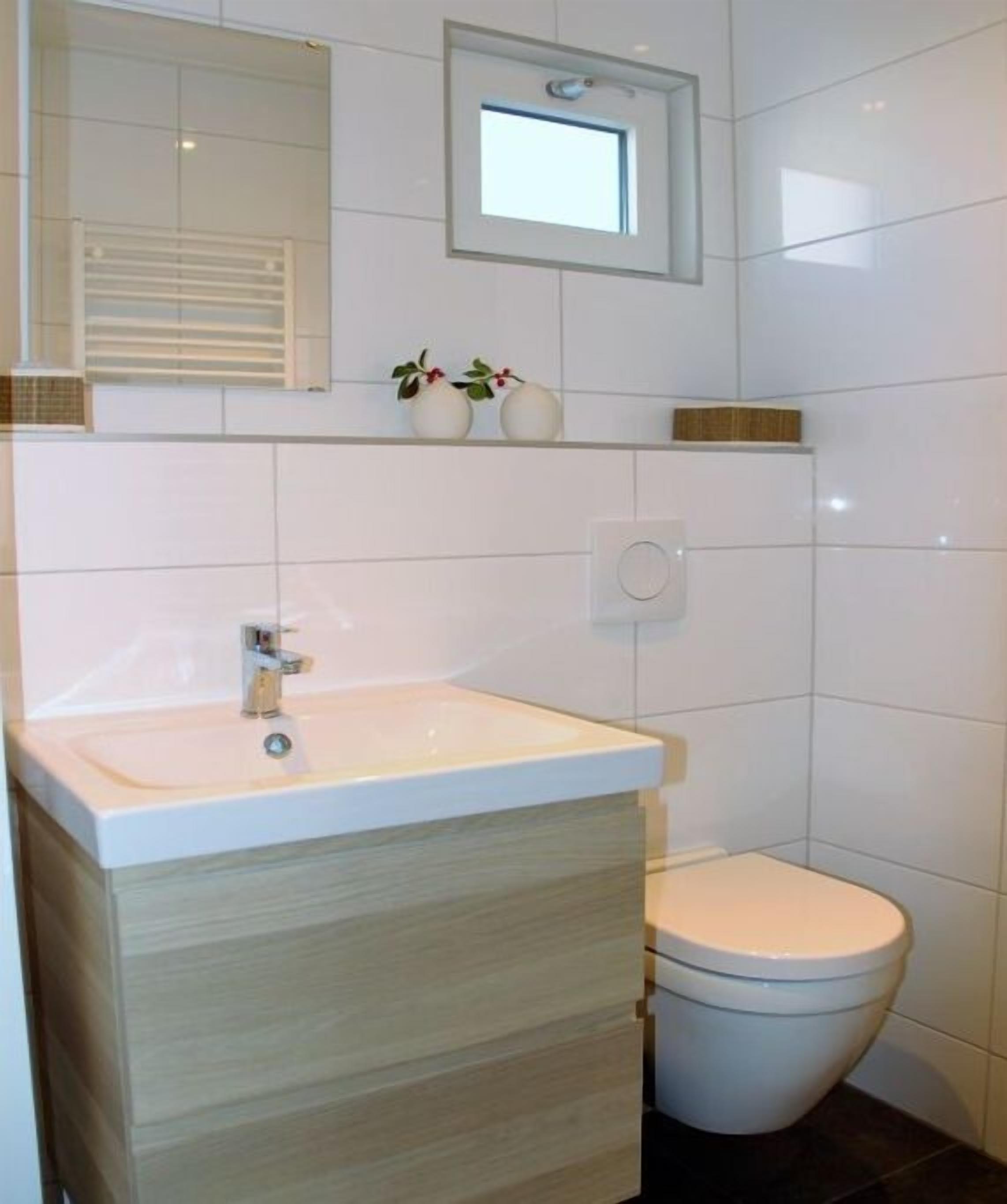 Et badeværelse med en hvid vask, et spejl, et toilet og et lille vindue.