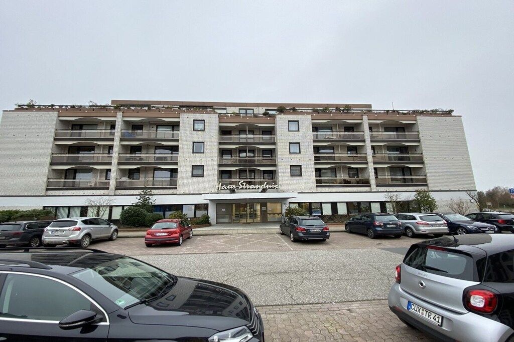 A multi-story hotel with a central entrance, parking lot, and several balconies.