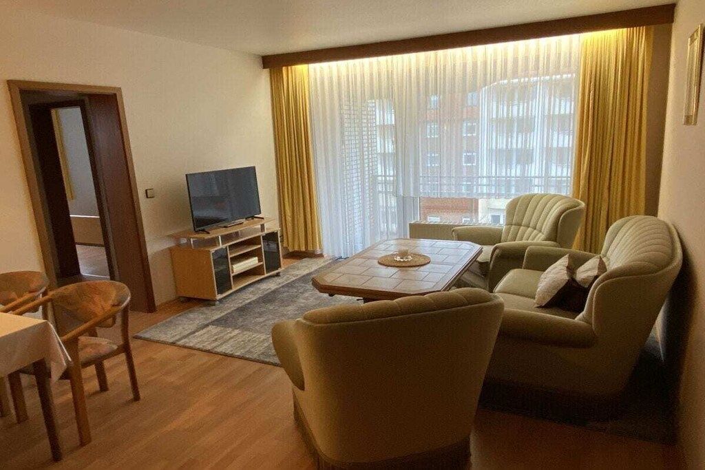 A hotel room with a television, two armchairs, a small table, and a dining area.