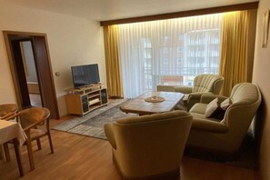 A hotel room with a television, two armchairs, a small table, and a dining area. - House Strandnixe No. 307 (Cuxhaven)