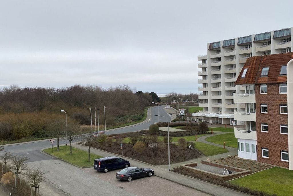 Een woongebied met een meerlaags appartementencomplex, een bochtige weg en een parkeerplaats met auto's.