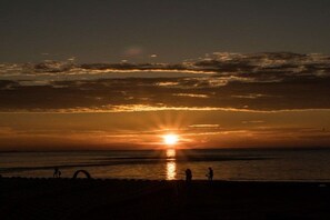 Ein Sonnenuntergang über einem Strand, mit Silhouetten von Menschen und einem klaren Himmel.