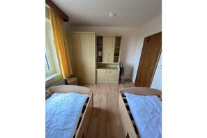 Ein Schlafzimmer mit zwei hölzernen Betten, einem Kleiderschrank und einem Fenster mit Vorhängen.