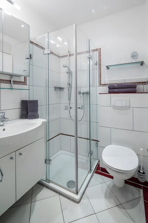 Ein modernes Badezimmer mit einer Duschkabine, einem weißen Waschbecken und einer Toilette.
