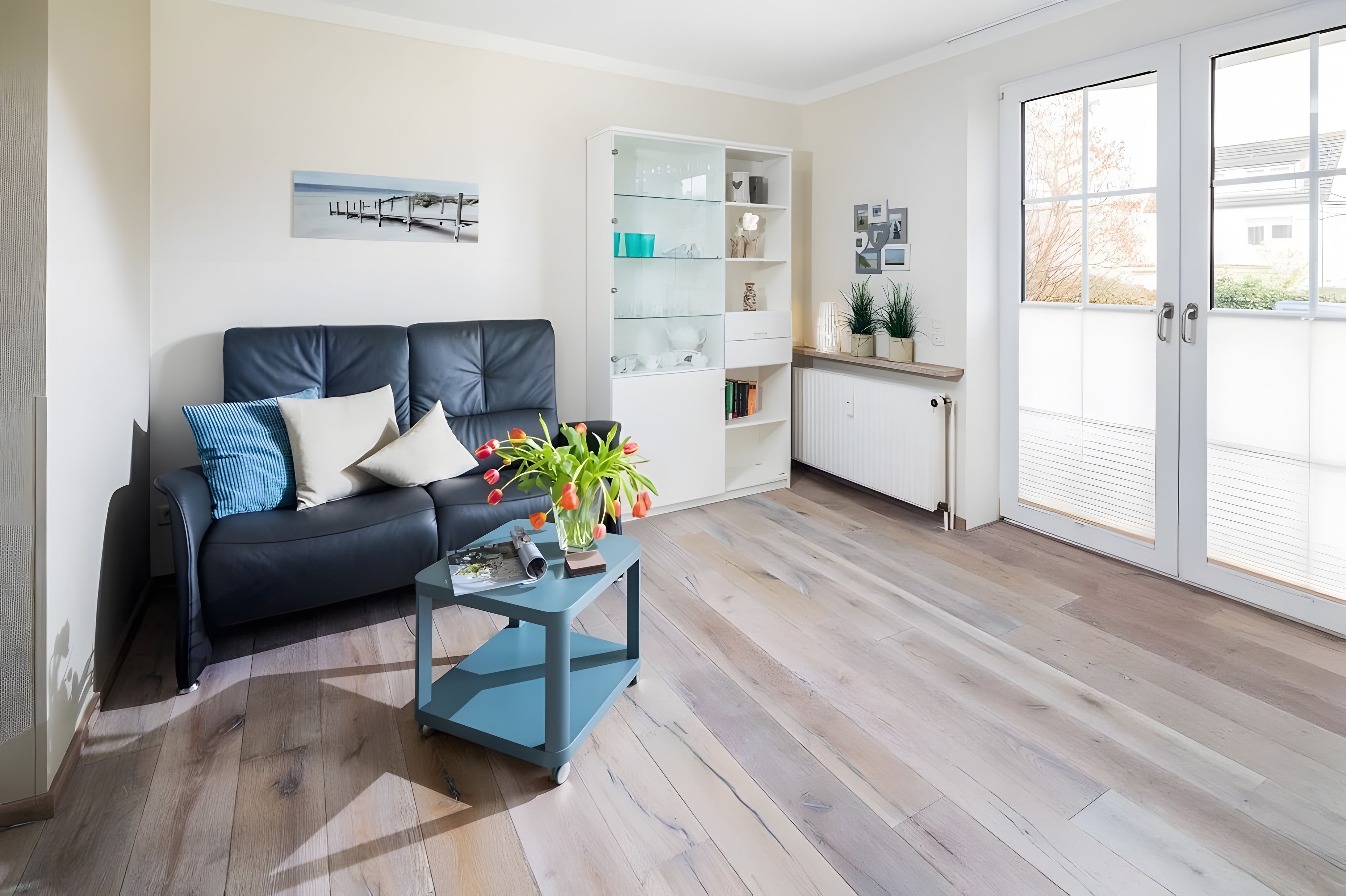 Ein modernes Wohnzimmer mit einem dunkel ledernen Sofa, einem Glastisch und Blick ins Freie durch große Schiebetüren.