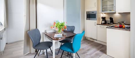 Une cuisine moderne avec un coin repas, comprenant une table avec des chaises, un vase avec des fleurs et une machine à café.
