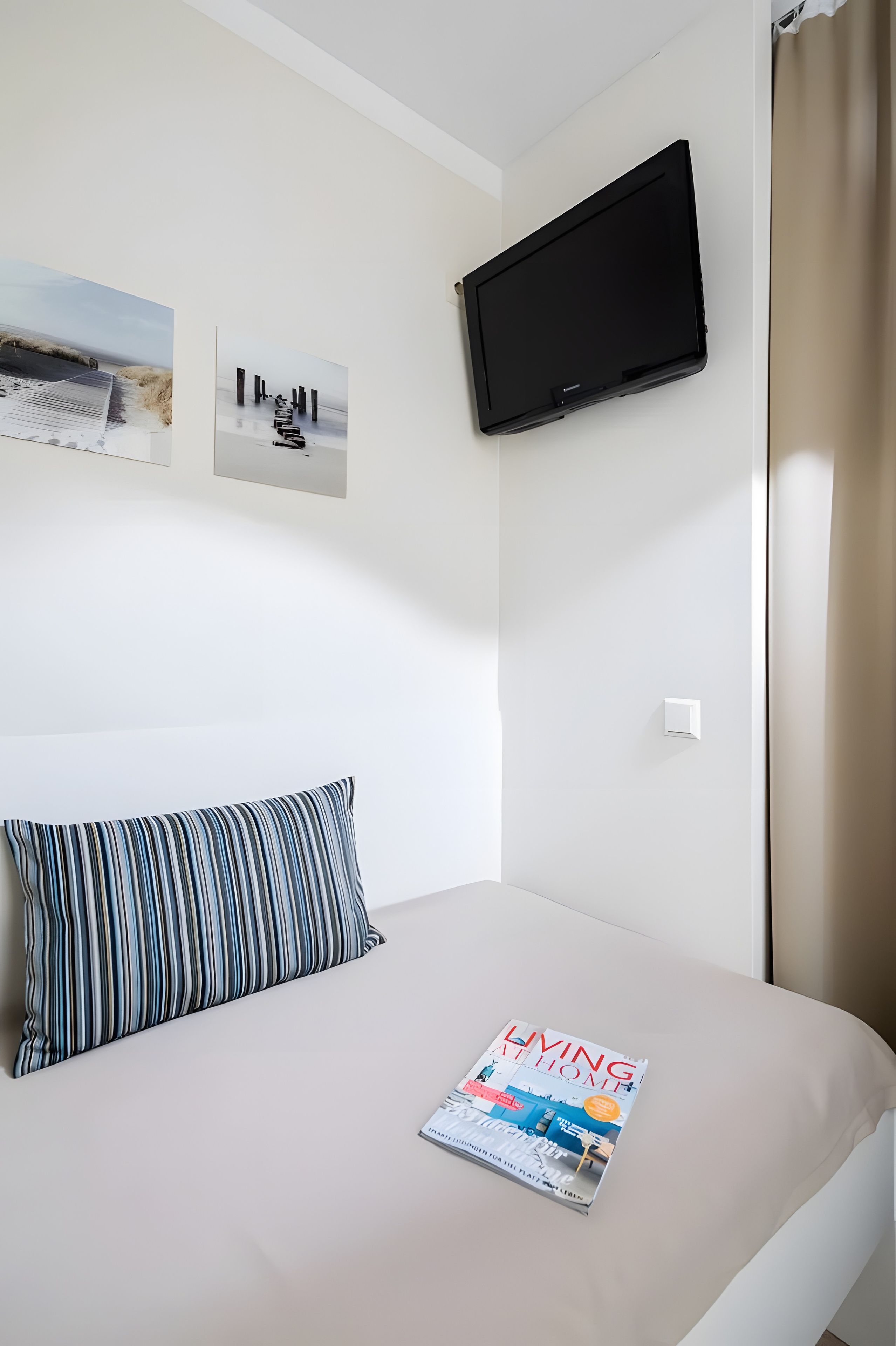 Ein Hotelzimmer mit einem Bett, einem an der Wand montierten Fernseher und einer Zeitschrift auf dem Bett.