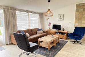A living room with a sofa, a coffee table, a TV stand, and a blue chair. - Previnaireweg 46 & 48 (Callantsoog)