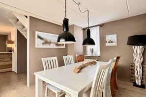 A dining area with a white table, chairs, and a hanging light fixture. - Holiday apartment with 1 bedroom (Callantsoog)