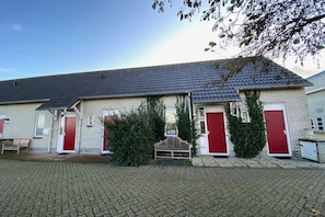 A building with a brick facade, red doors, and a paved courtyard. - Holiday apartment with 1 bedroom (Callantsoog)