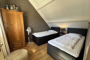 A bedroom with two beds, a wooden wardrobe, a fan, and a lamp. - Holiday apartment with 1 bedroom (Callantsoog)