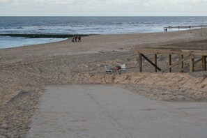 A beach with a wooden walkway, a few beach chairs, and people in the distance. - Bungalow with 1 bedroom (Callantsoog)