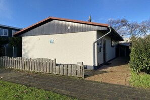 A building with a white exterior, a brown roof, and a wooden fence in front. - Bungalow with 1 bedroom (Callantsoog)