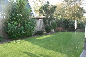 A well-maintained backyard with a wooden fence, a small shed, and a variety of shrubs and trees. - Bungalow with 1 bedroom (Callantsoog)
