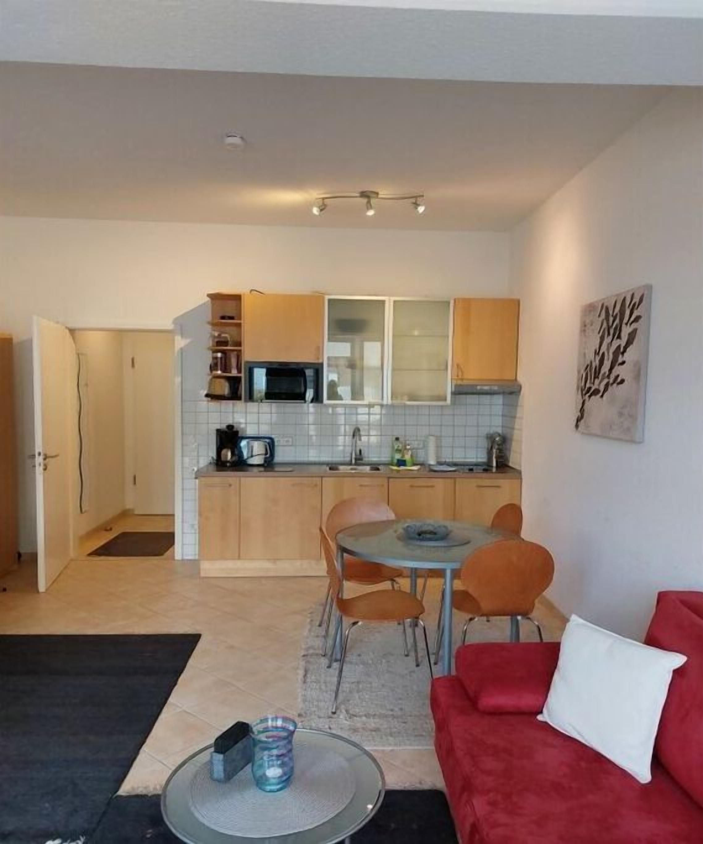 Un espacio habitable pequeño con kitchenette, zona de comedor y sofá rojo.