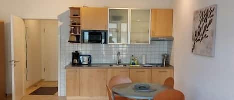 Un espacio habitable pequeño con kitchenette, zona de comedor y sofá rojo.