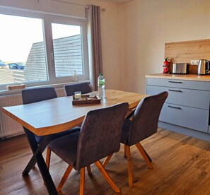 A modern kitchen with a wooden table and chairs, a window with curtains, and a view of the outside.