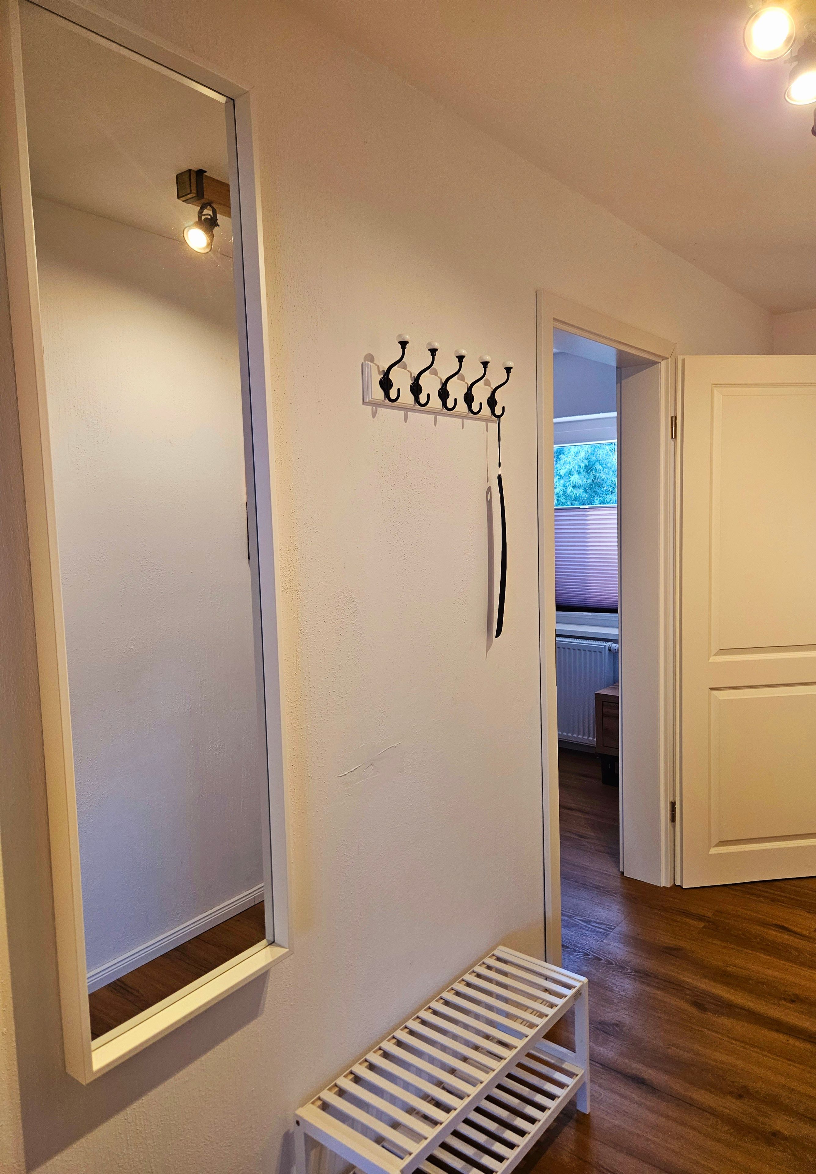 Ein Zimmer mit einem großen Spiegel, einem Kleiderhaken und einer Bank.