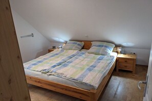 Yhden hengen sänky, jossa on ruutukuviollinen peitto, kaksi yöpöytää, joissa on lamput, ja puinen pääty.