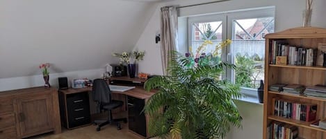 A room with a desk, chair, bookshelf, potted plant, and a window with a view of buildings.